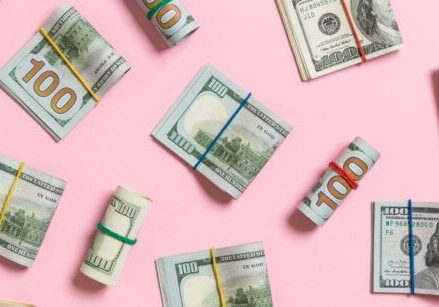 folded and rolled-up bundles of money on a pink background