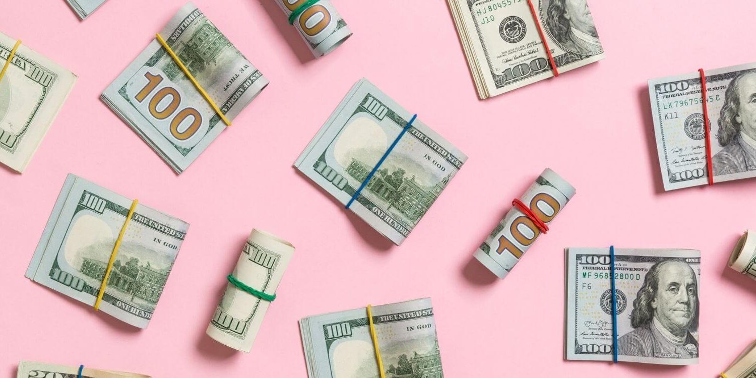 folded and rolled-up bundles of money on a pink background