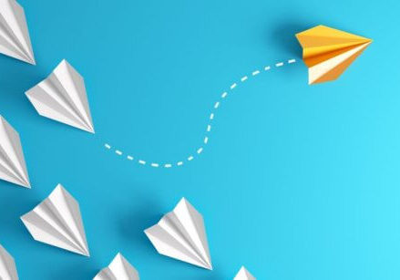 white paper airplanes flying in formation on a blue background with one yellow paper airplane breaking from the formation