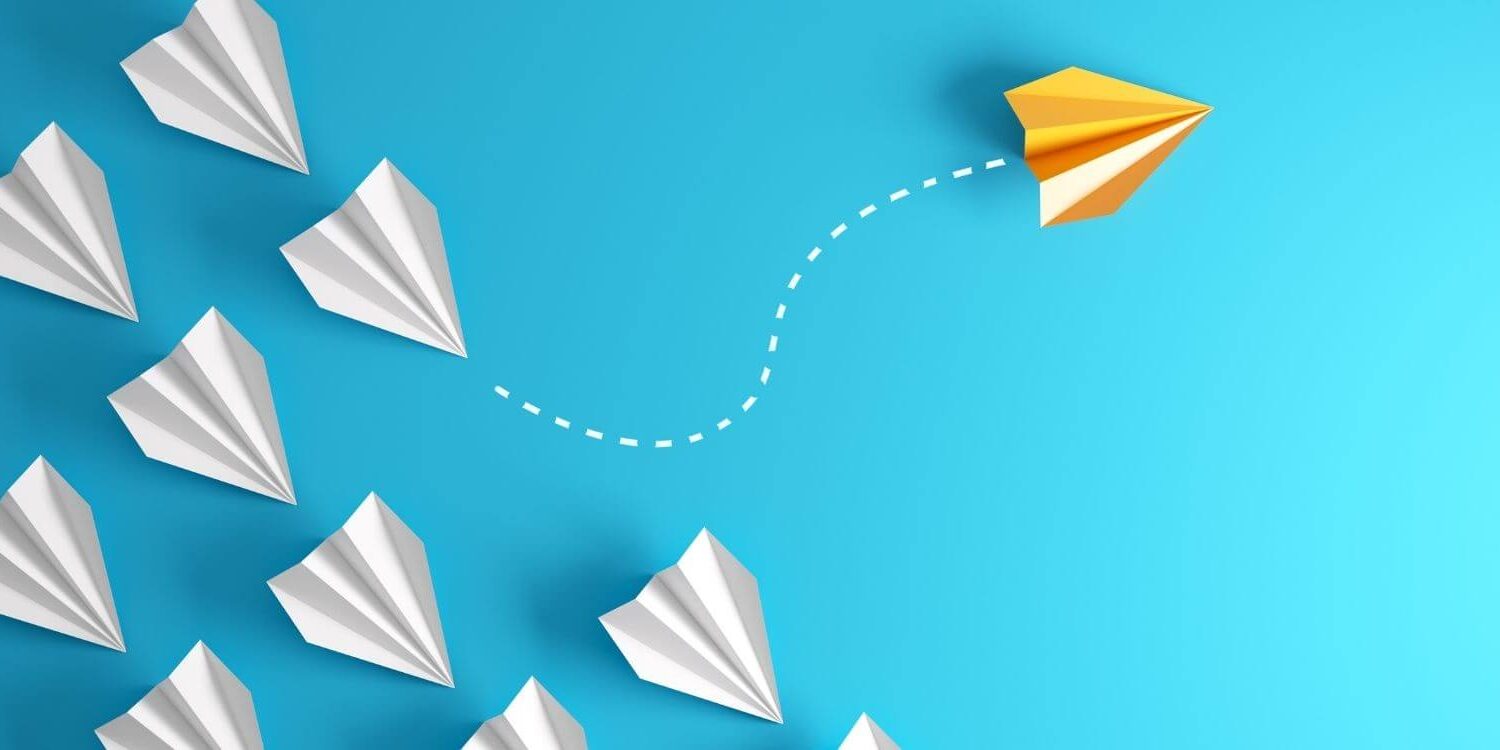 white paper airplanes flying in formation on a blue background with one yellow paper airplane breaking from the formation