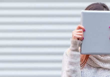 woman holding a laptop or an ipad against her face, hiding behind it.