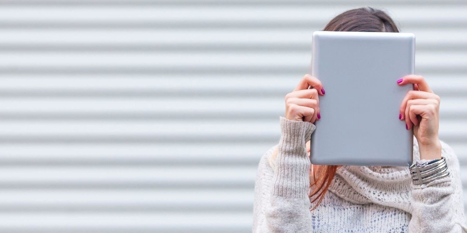 woman holding a laptop or an ipad against her face, hiding behind it.