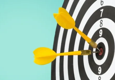 black and white bullseye with yellow darts hitting the center on a turquoise background