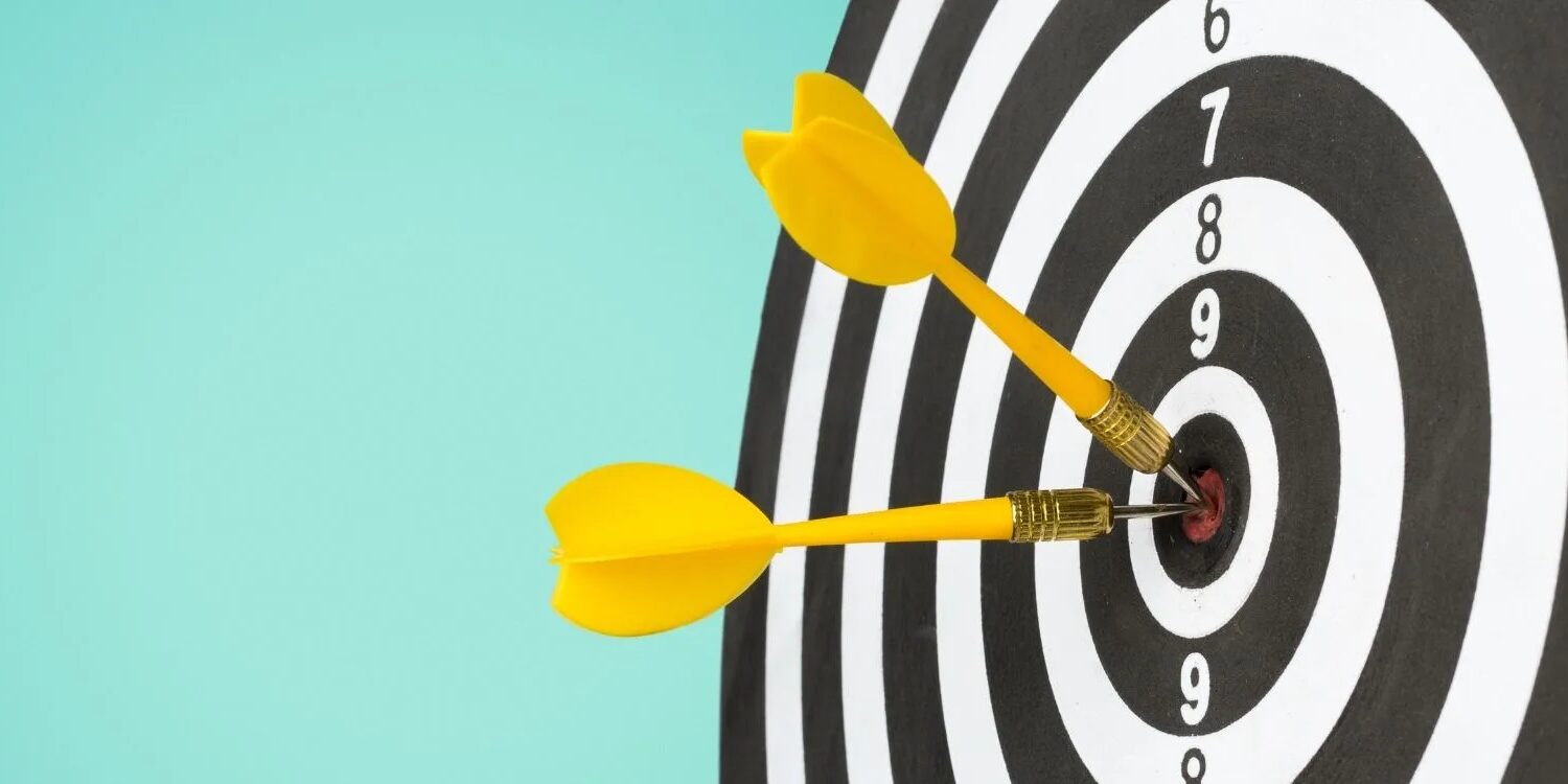 black and white bullseye with yellow darts hitting the center on a turquoise background