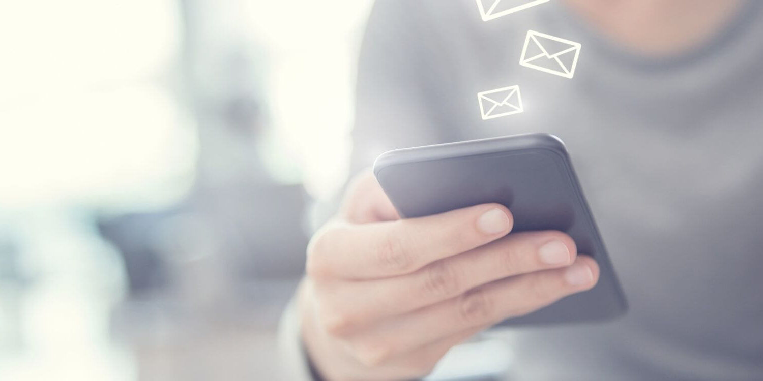 woman wearing a gray sweater holding a phone with email envelopes floating up from the device