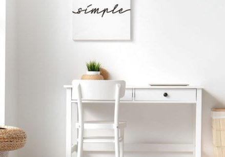 minimalist desk against white wall with a white framed picture that says simple on it with black letters