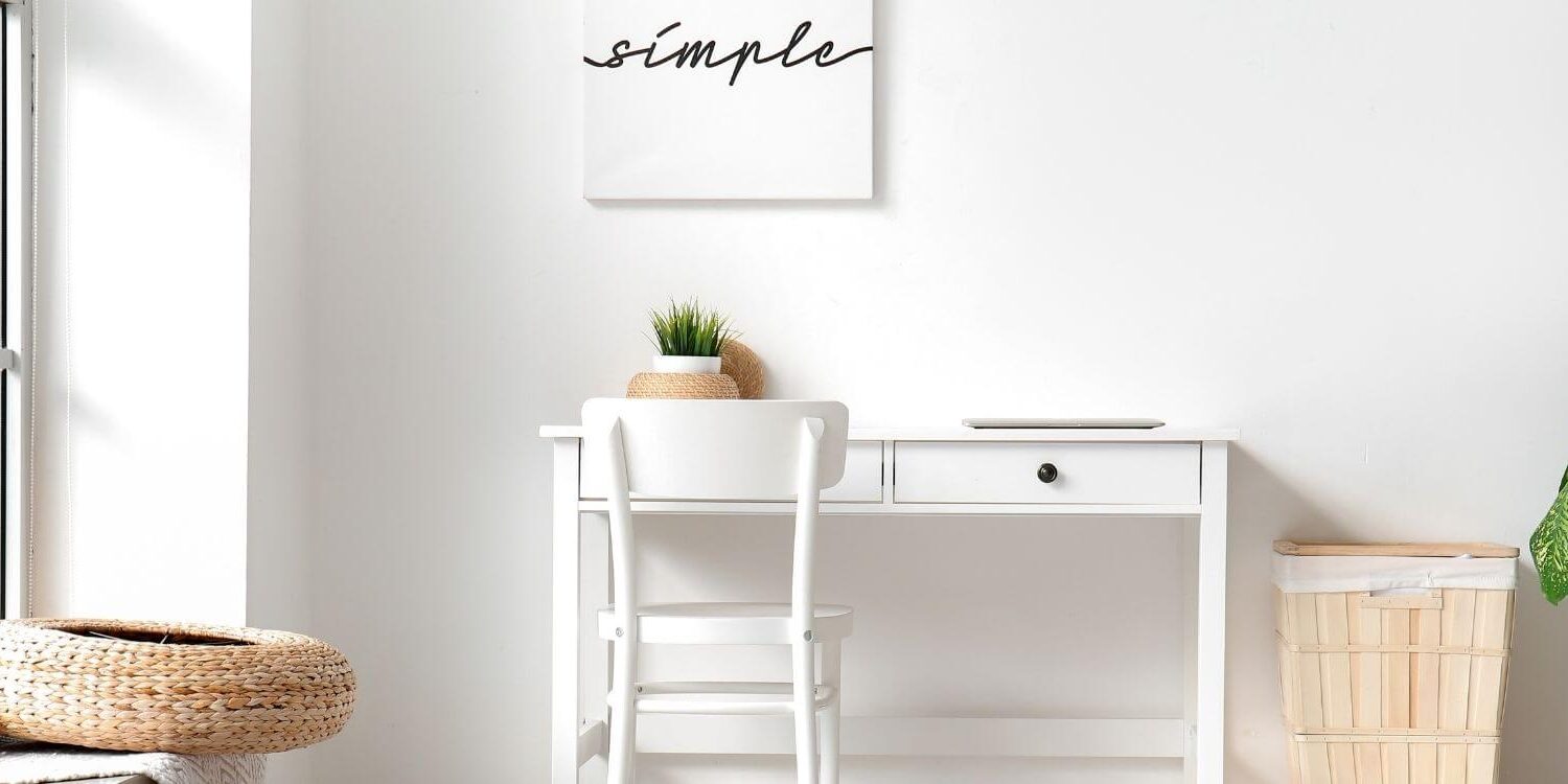 minimalist desk against white wall with a white framed picture that says simple on it with black letters