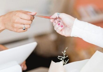 one woman handing a credit card to another woman at a checkout counter