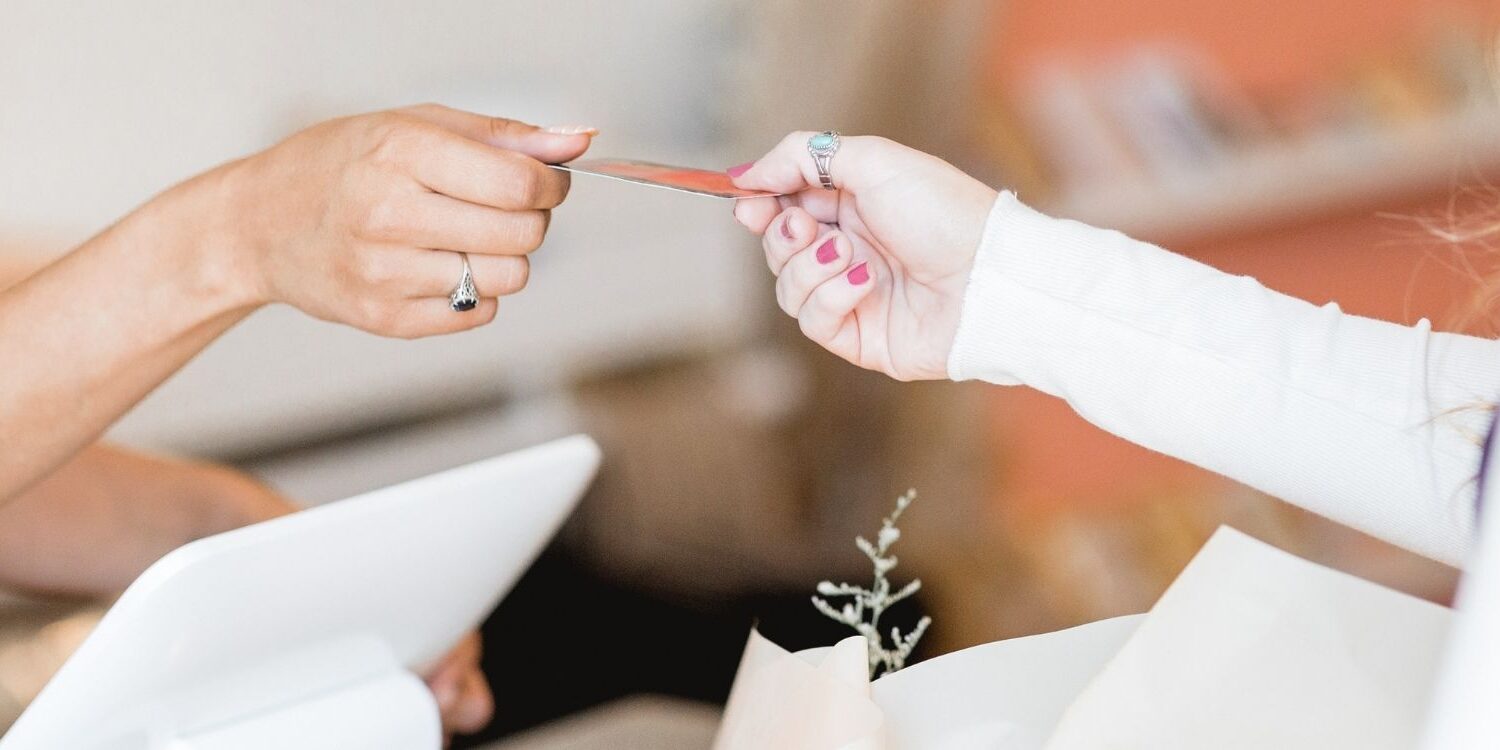 one woman handing a credit card to another woman at a checkout counter