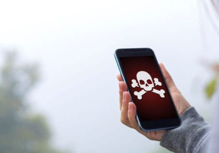 woman holding a cell phone with a skull and cross bones on the screen showing her website was hacked