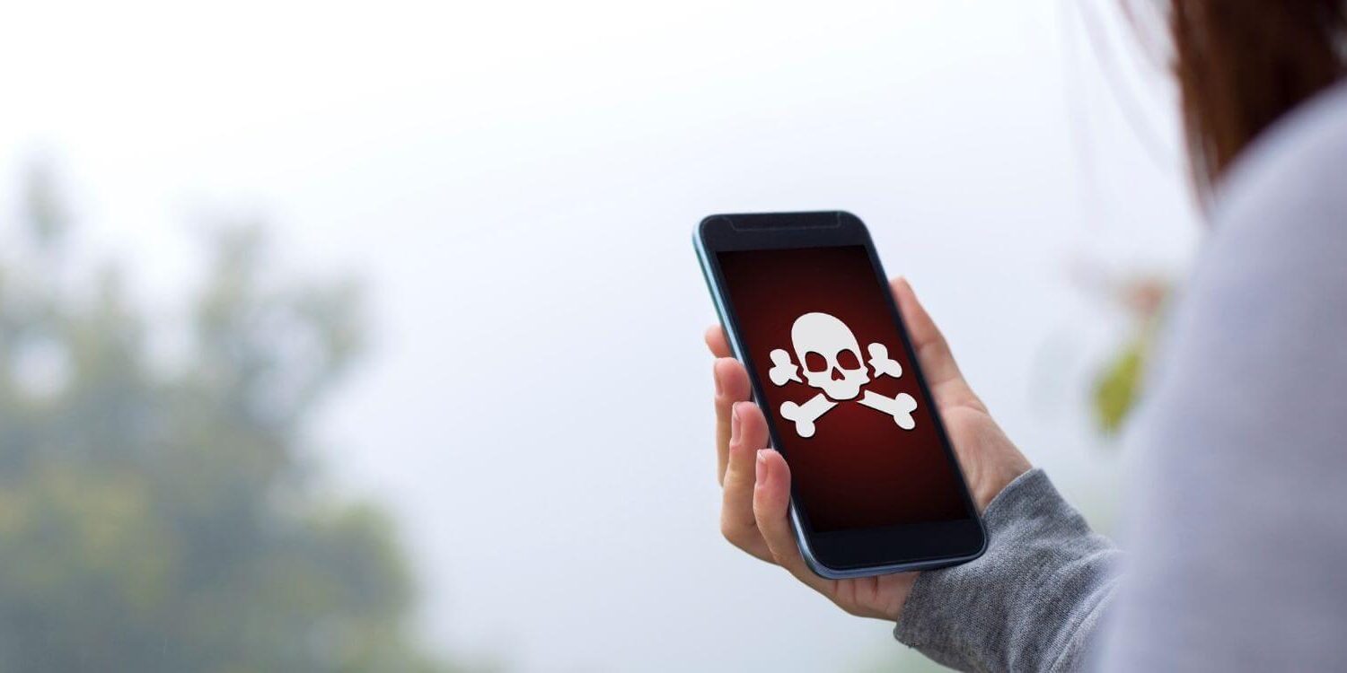 woman holding a cell phone with a skull and cross bones on the screen showing her website was hacked