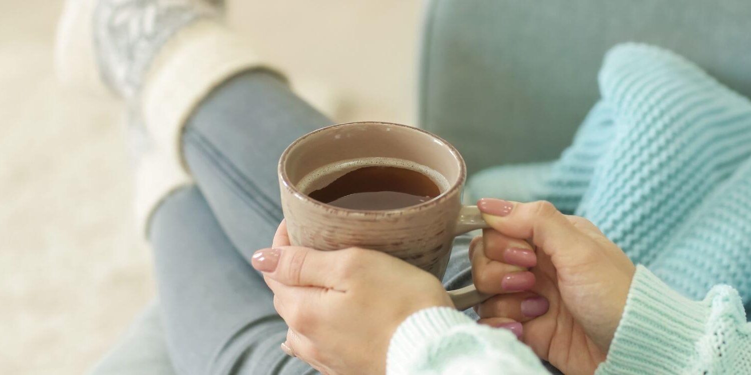 woman relaxing on a sofa wearing fuzzy socks and holding a warm cup of coffee or tea