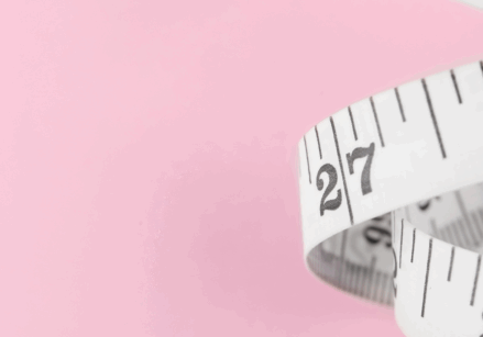 A white flexible tape measure on a pink background representing measuring your marketing metrics.