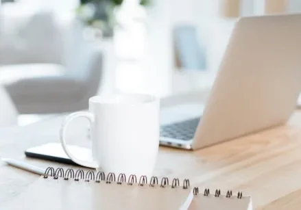 still life photo of a laptop, mug, and notebook