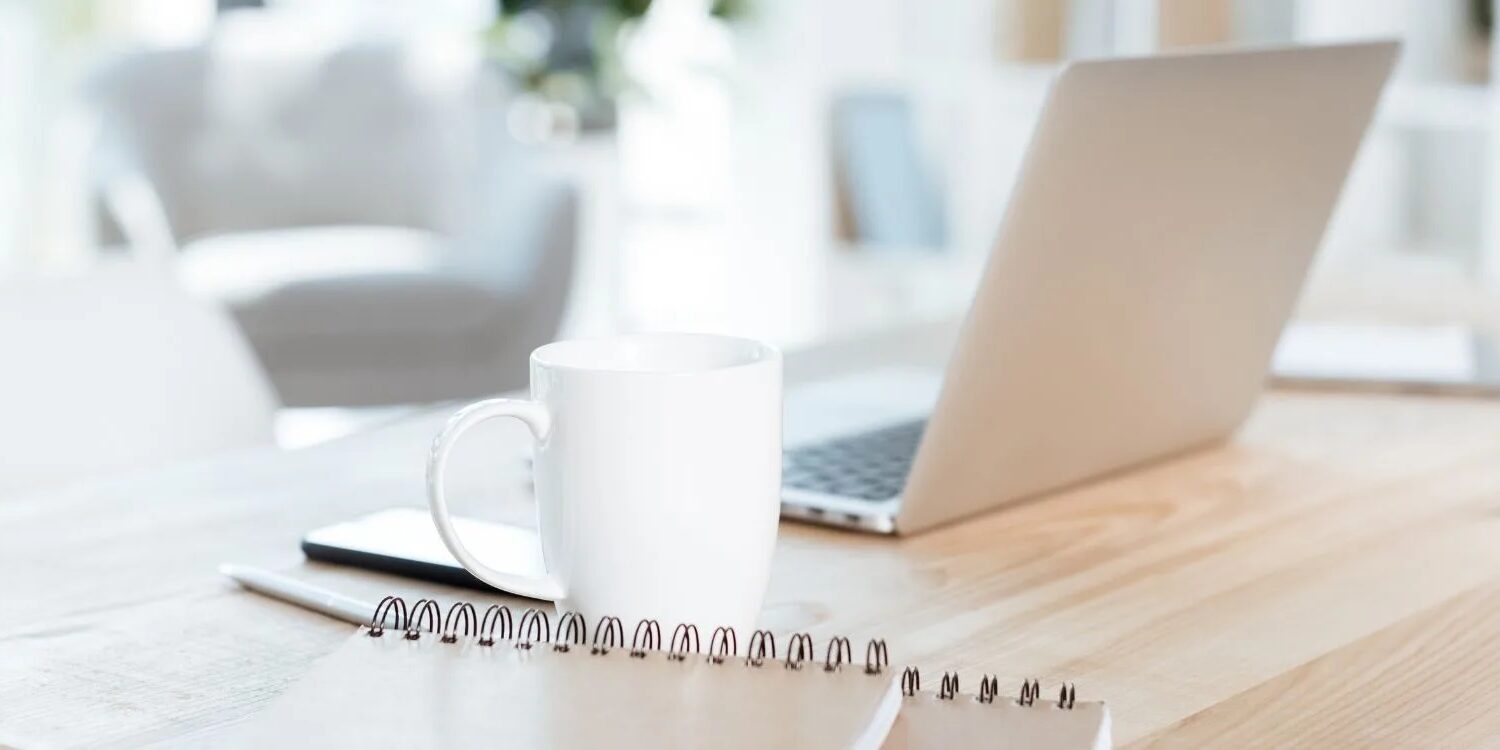 still life photo of a laptop, mug, and notebook