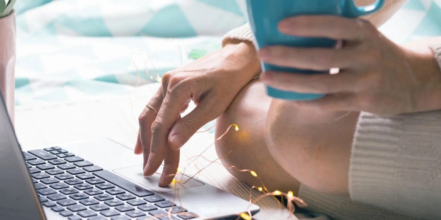 woman sitting on the floor typing on a laptop with one hand and holding a turquoise coffee mug with the other hand