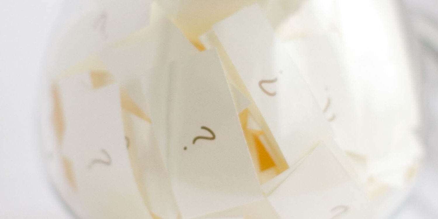 Clear glass jar with slips of paper with question marks written on them.
