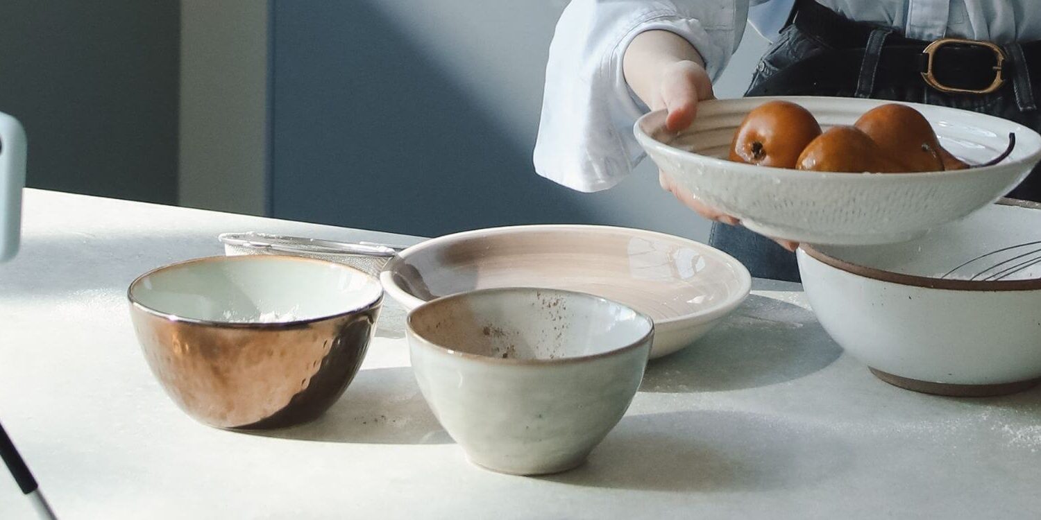 woman recording a video of herself making a batch of cookies with her cellphone on a tripod on the counter with a bunch of bowls full of ingredients