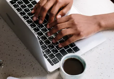 Hands typing on a keyboard to create a speedy blog post, with a cup of coffee to the side.