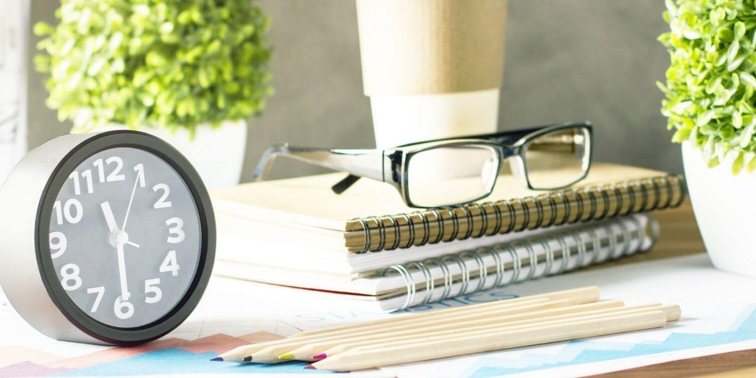 pile of notebooks with glasses on top of them next to a clock with a couple of plants in the background