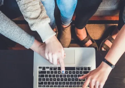 The hands of three people pointing at a laptop