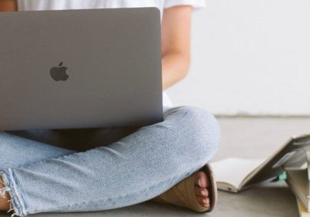 Woman holding a laptop sitting on the floor with a coffee mug on a stack of books