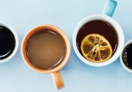 a row of 6 mugs on a blue table photographed from above with different types of drinks inside each mug