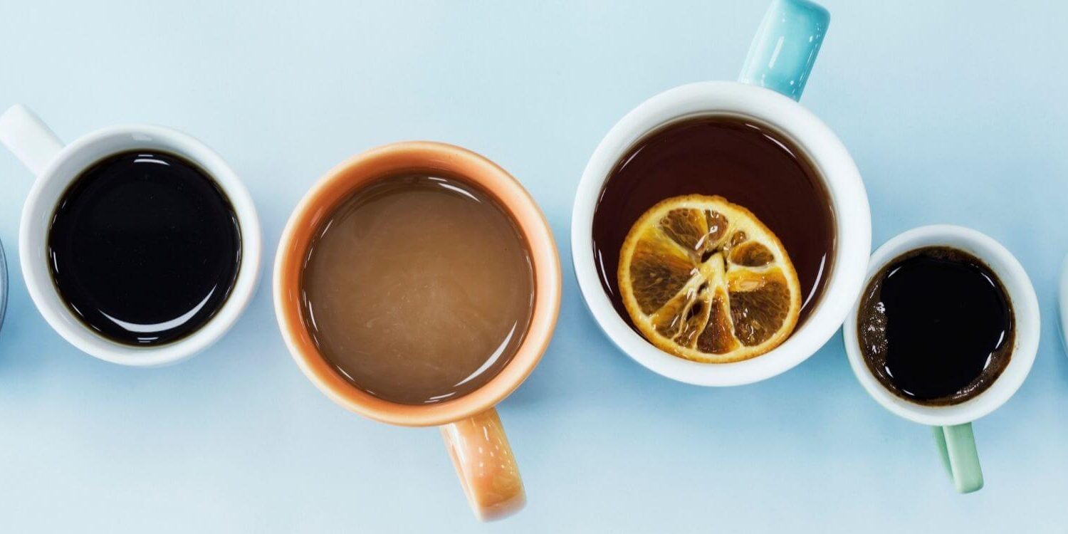 a row of 6 mugs on a blue table photographed from above with different types of drinks inside each mug