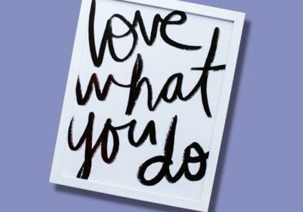 white framed sign with "love what you do" painted on a white background. the frame is laying on a purple background