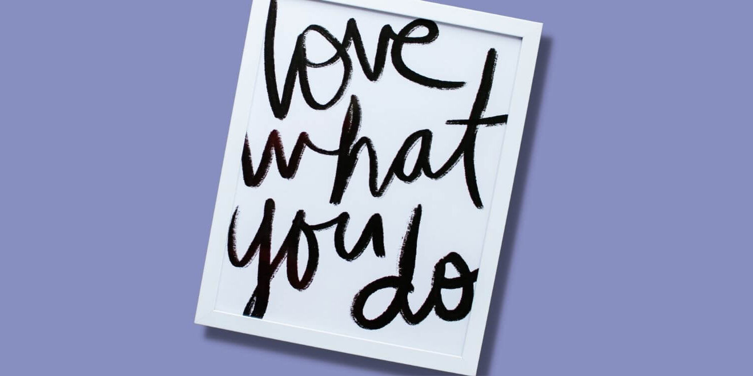 white framed sign with "love what you do" painted on a white background. the frame is laying on a purple background
