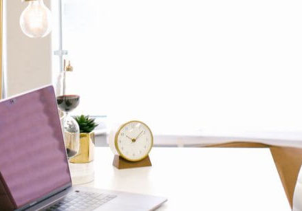 pretty desk in front of a window with a laptop, clock, white desk chair, etc.