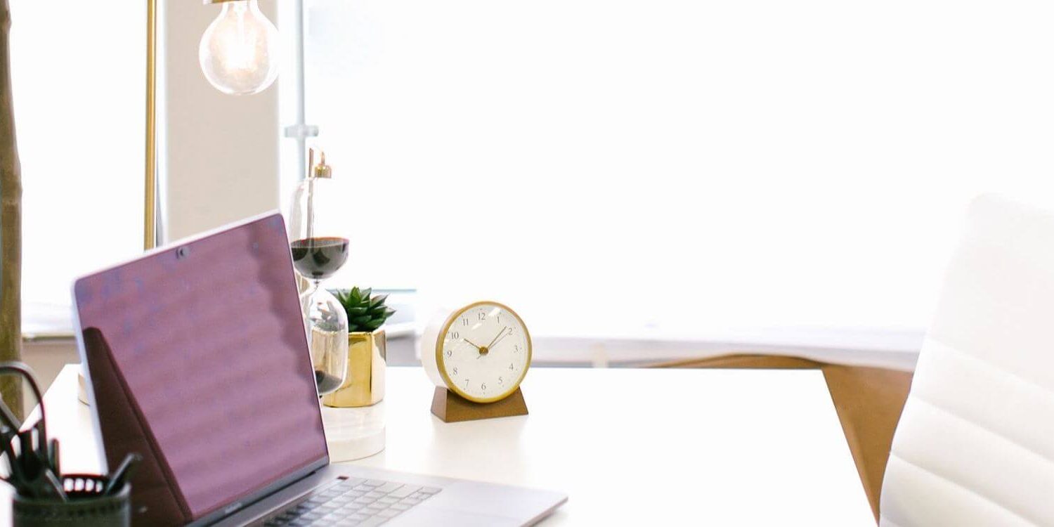 pretty desk in front of a window with a laptop, clock, white desk chair, etc.