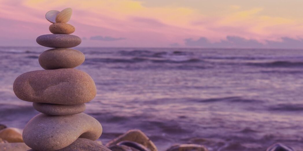a stack of rocks balanced against an ocean at sunset - representing balanced not busy