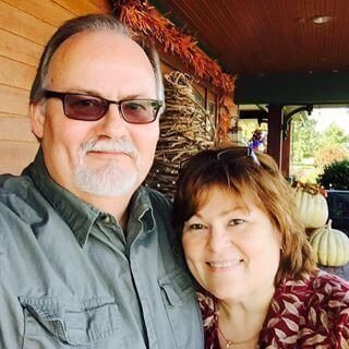 man with sunglasses and gray beard standing next to woman with auburn hair.