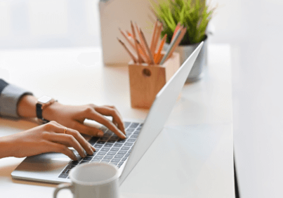woman creating content, typing on a laptop, with a coffee mug on her desk.