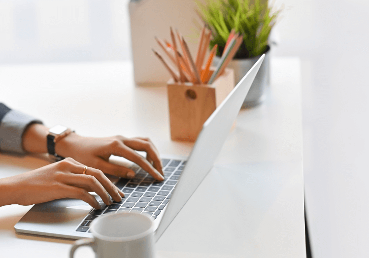 woman creating content, typing on a laptop, with a coffee mug on her desk.