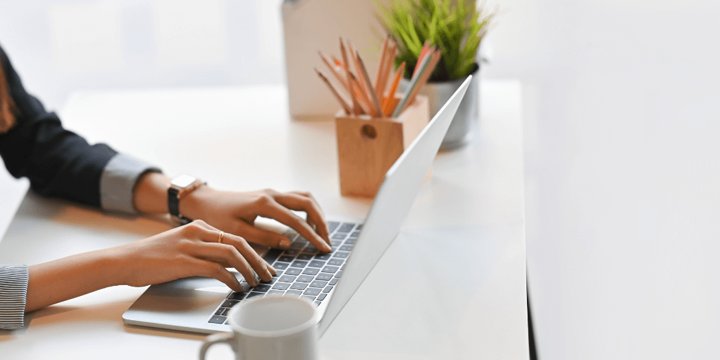 woman creating content, typing on a laptop, with a coffee mug on her desk.
