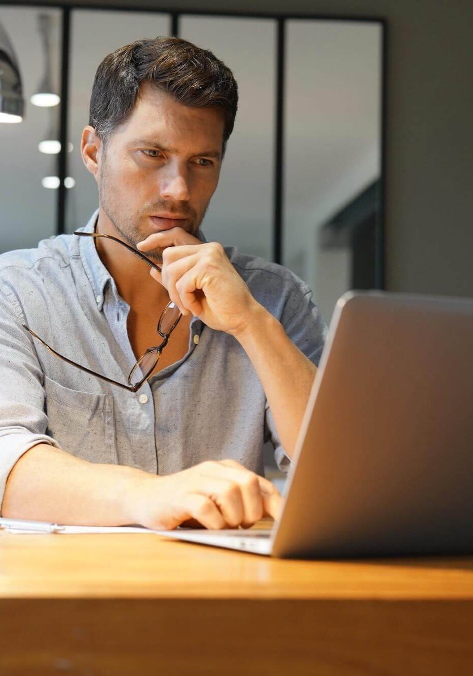 middle age man holding glasses working on laptop