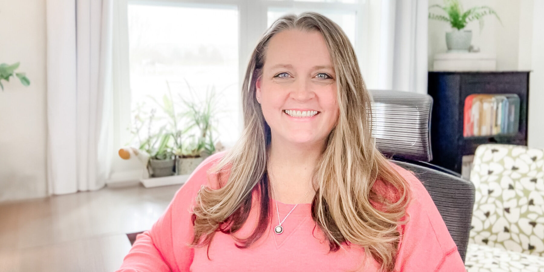 heather stephens: woman with long brown hair wearing a pink sweatshirt sitting at her desk.