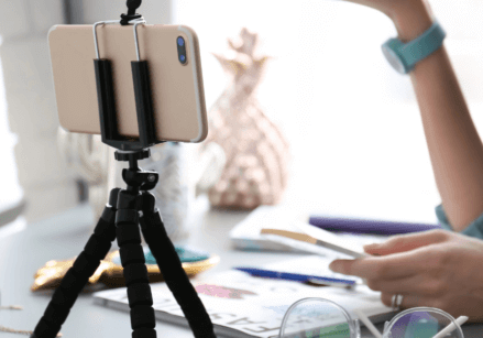 image of a phone in a tripod on a desk with a woman in the background recording a video