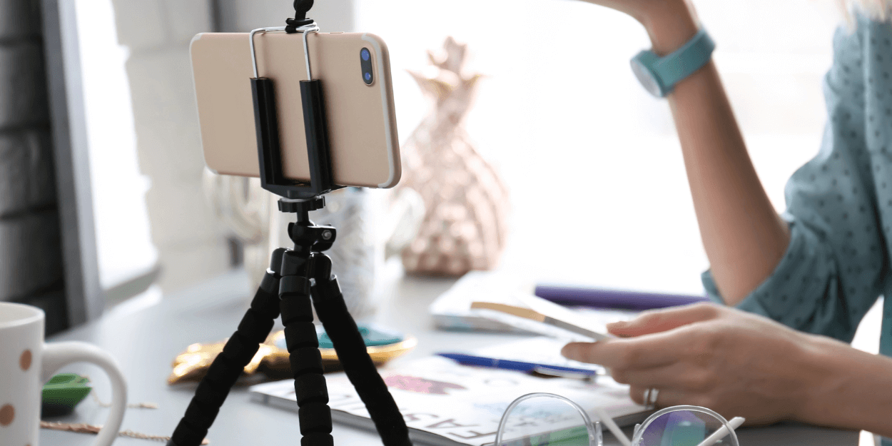 image of a phone in a tripod on a desk with a woman in the background recording a video