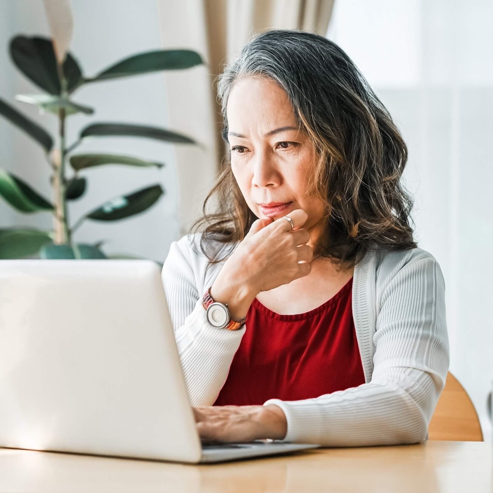 A woman business owner working at a laptop with a plant in the background.