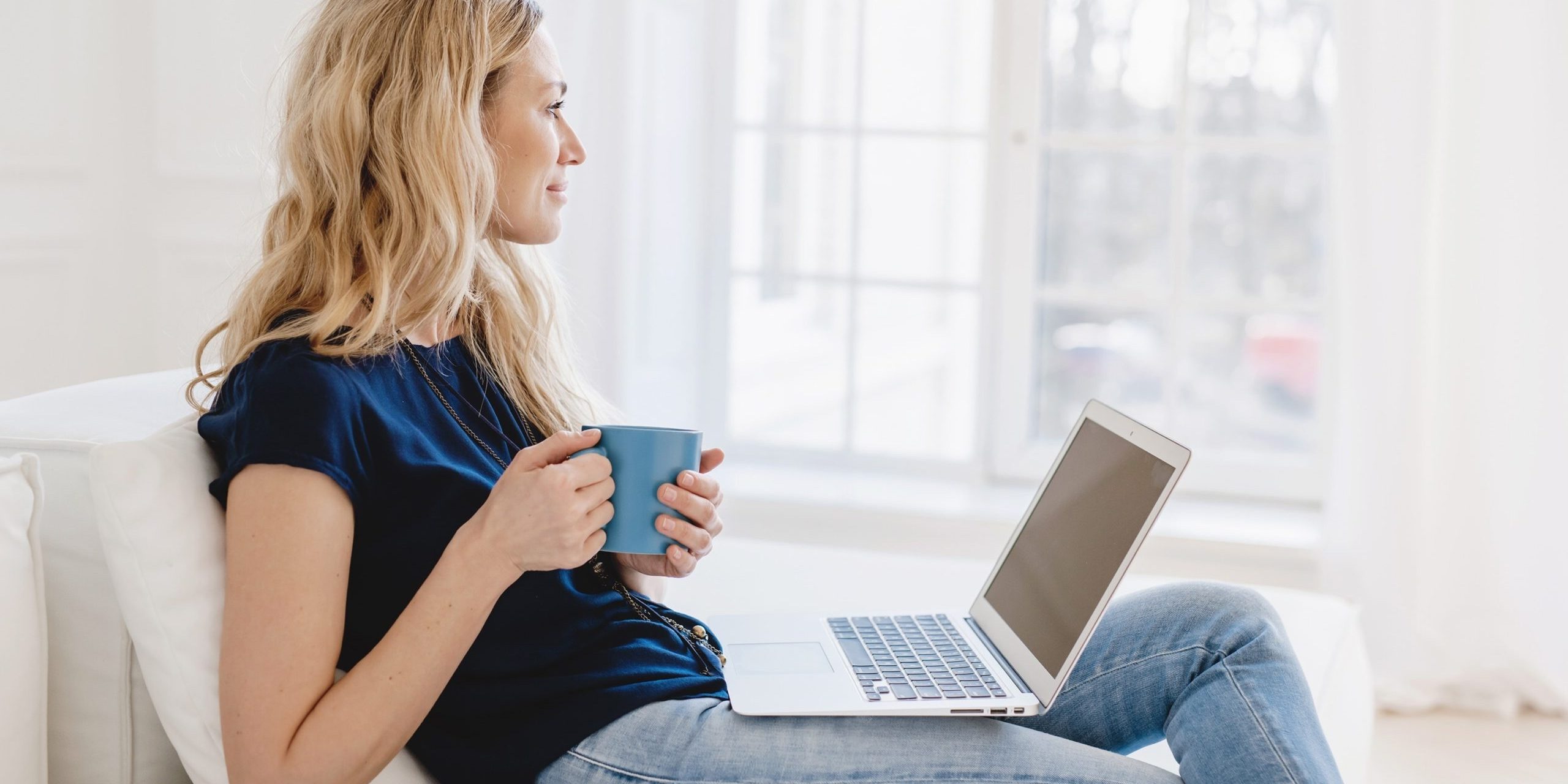Woman sitting peacefully with her open holding coffee gazing out the window.